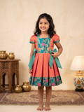 Happy young girl enjoying her premium coral and teal brocade silk knee-length ethnic frock dress inside a warm cream room- House of Kritee