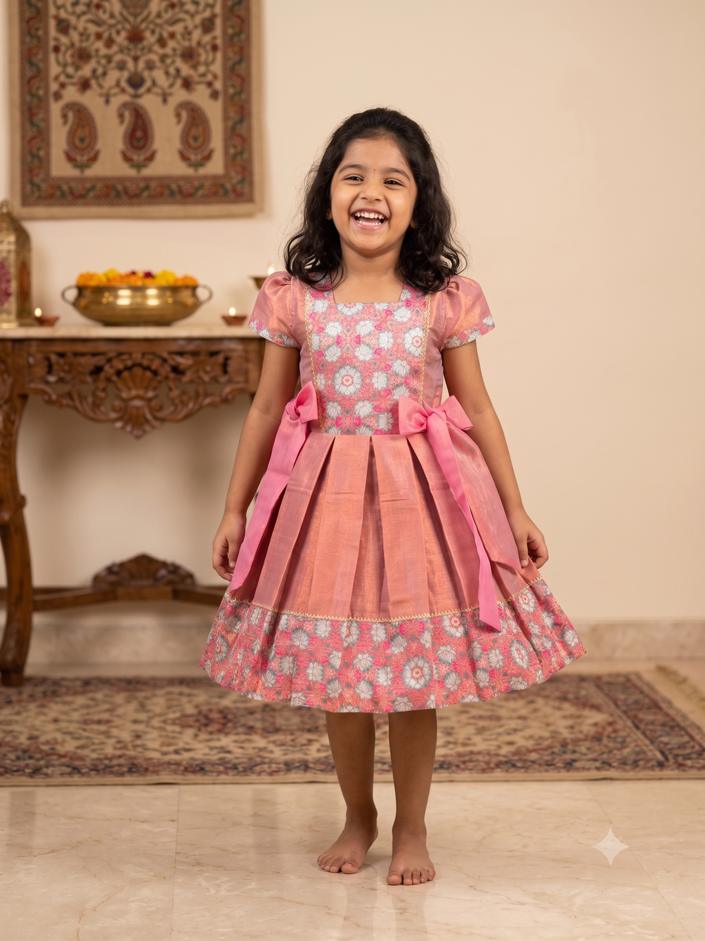 Happy young girl wearing a premium peach and pink floral brocade silk knee-length ethnic frock dress inside a warm cream room - House of Kritee