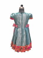 A short-sleeve teal blue dress displayed on a mannequin, featuring pink bow accents at the waist and a pink floral patterned hem. - House of Kritee