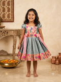 Happy young girl enjoying her premium blue and peach peacock motif silk knee-length ethnic frock inside a warm cream room - House of Kritee