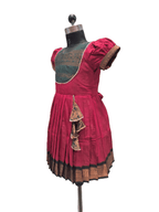 A traditional Indian salwar suit displayed on a dress form mannequin, featuring a deep magenta pink pleated skirt with a black and gold border, a dark green embroidered yoke, and matching pink puff sleeves. - House of Kritee