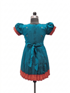 A teal blue cotton dress displayed on a mannequin, featuring puff sleeves with red cuffs, a matching waist tie, and a red patterned hem.