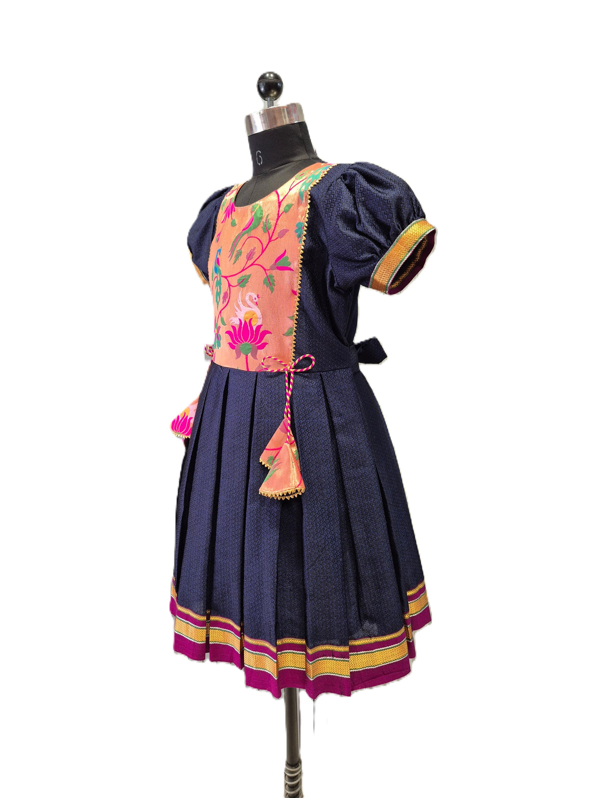 A traditional short-sleeve dress displayed on a mannequin against a white background. The dress features a navy blue skirt and sleeves, a peach-colored embroidered bodice with floral patterns, and gold and pink trim details. - House of Kritee
