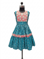 A sleeveless teal blue dress displayed on a black dress form mannequin, featuring a heavily embroidered coral pink and cream floral yoke and a tiered skirt with a matching coral pink band.
